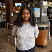 A young African American woman in a white blouse stands in a college cafeteria. 