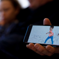 A phone shows a photo of a toddler running on a beach. The same girl, now 11, sits behind the phone. 
