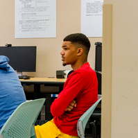 Two African American men sit in chairs in a classroom. 