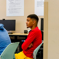 Two African American men sit in chairs in a classroom. 