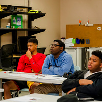 Young African American men sit at their desks in a classroom. 