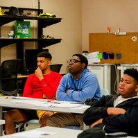 Young African American men sit at their desks in a classroom. 