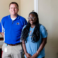 Young African American woman wears braids and stands with one of her instructors. 
