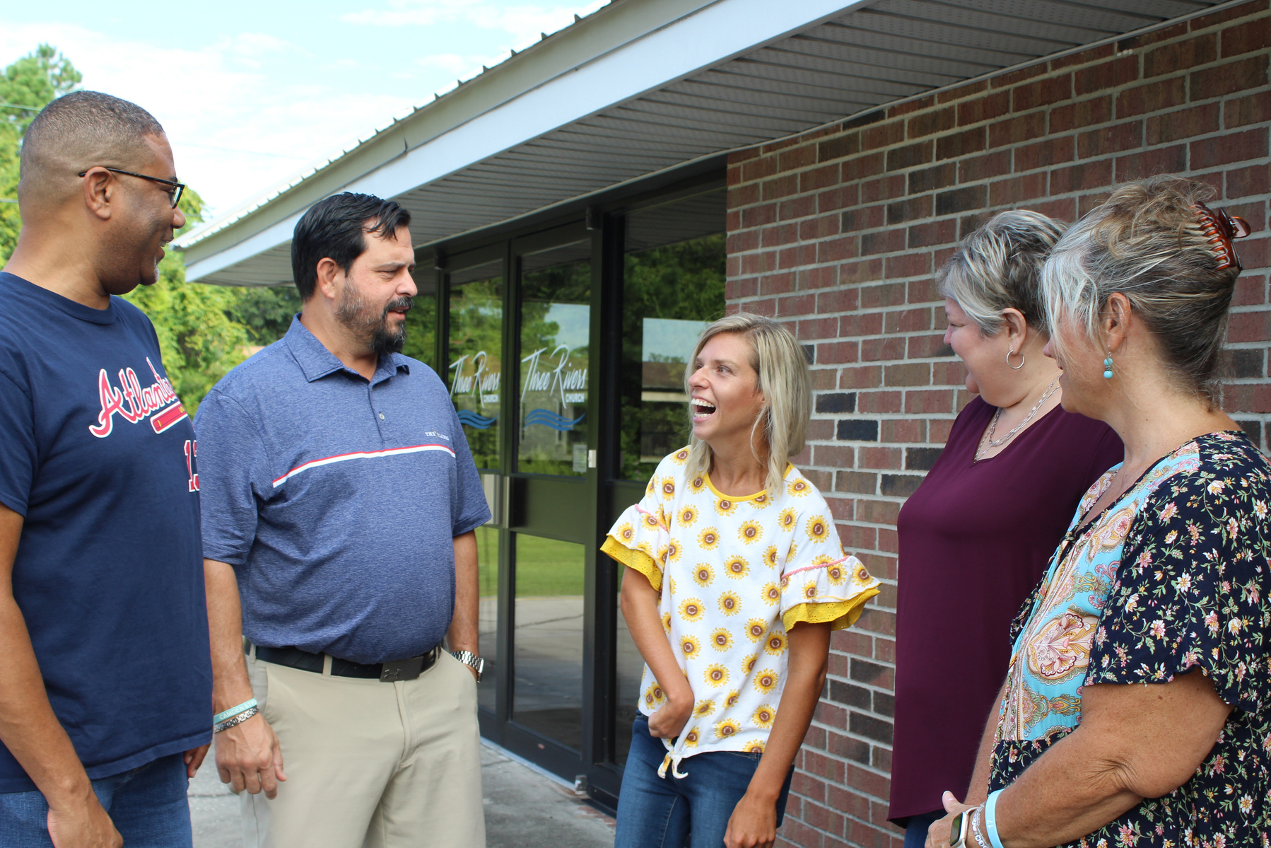 Five people stand in front of a brick building and talk. 