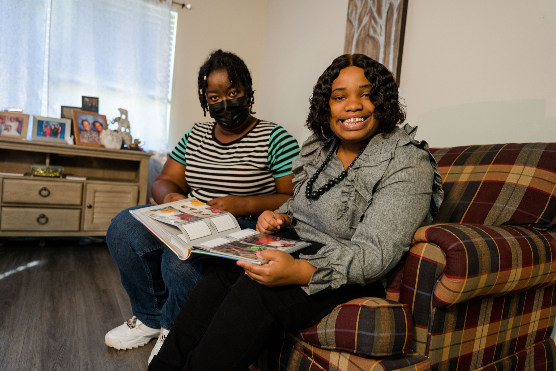 Two women sit close together on a sofa inside a home. 