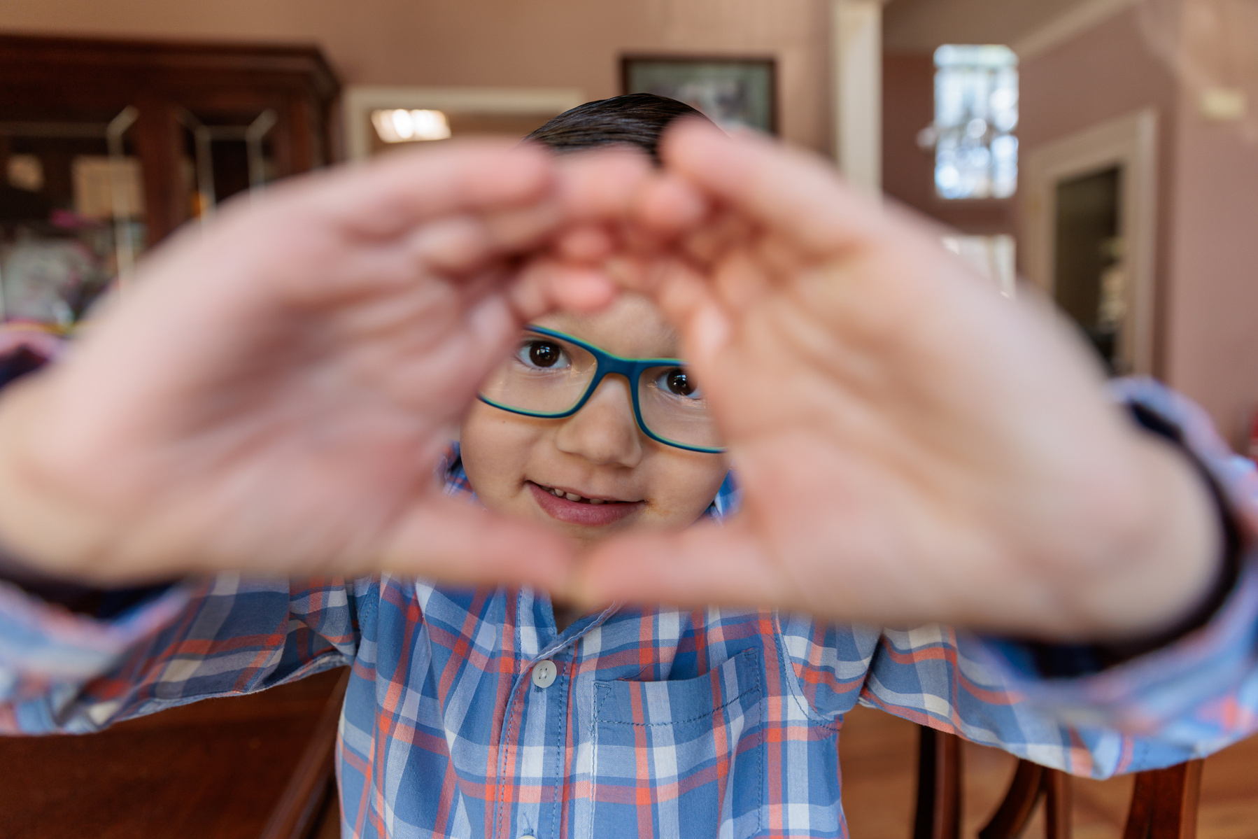 Small boy in a plaid shirt and glasses makes a square shape with his hands
