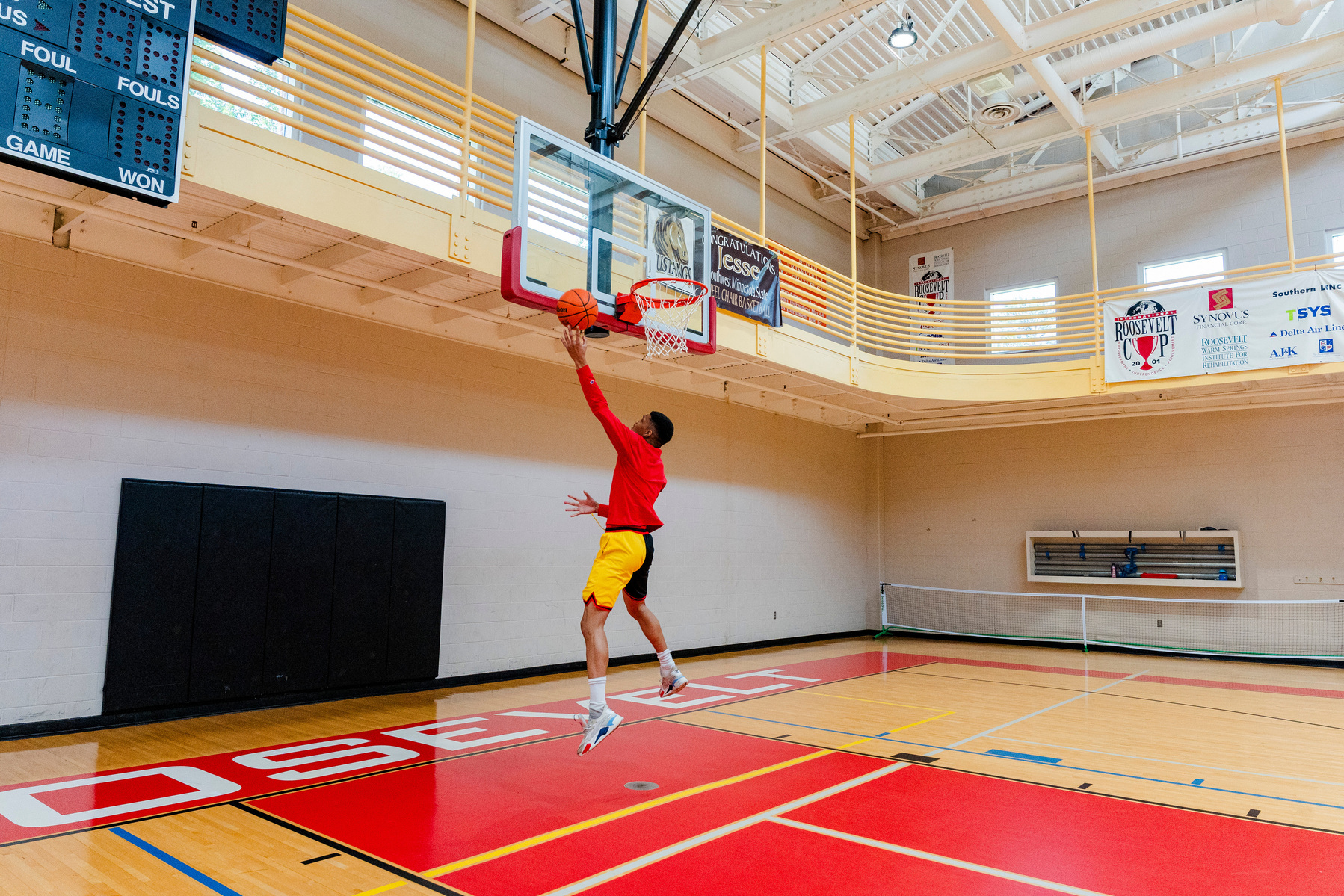 A man wears a bright red shirt while playing basketball in a gymnasium. 