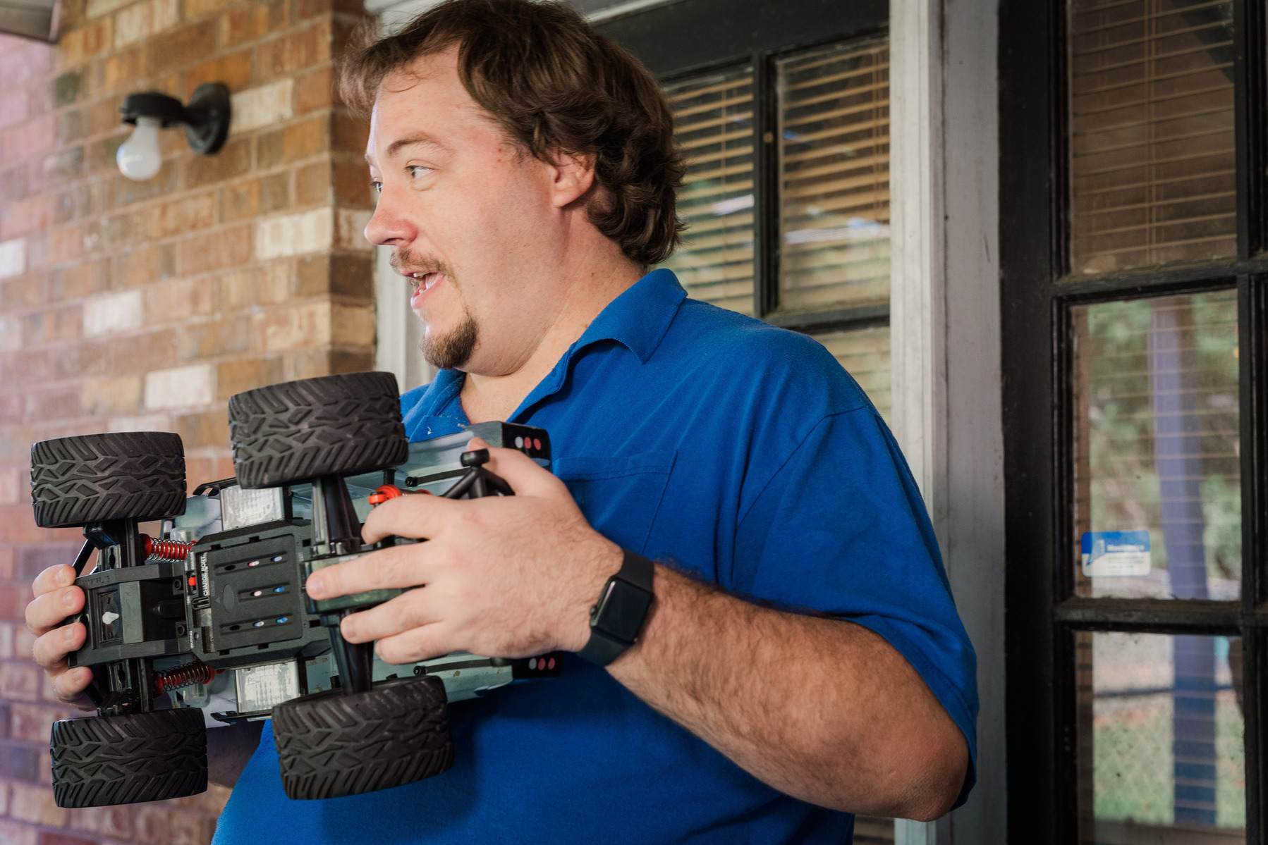 A man in a blue polo shirt holds a remote-controlled truck. 
