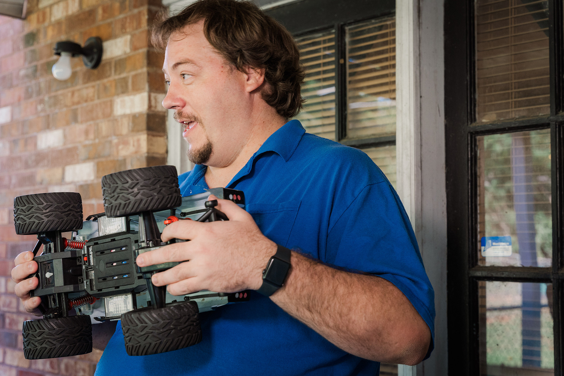 A man in a blue polo shirt holds a remote-controlled truck. 