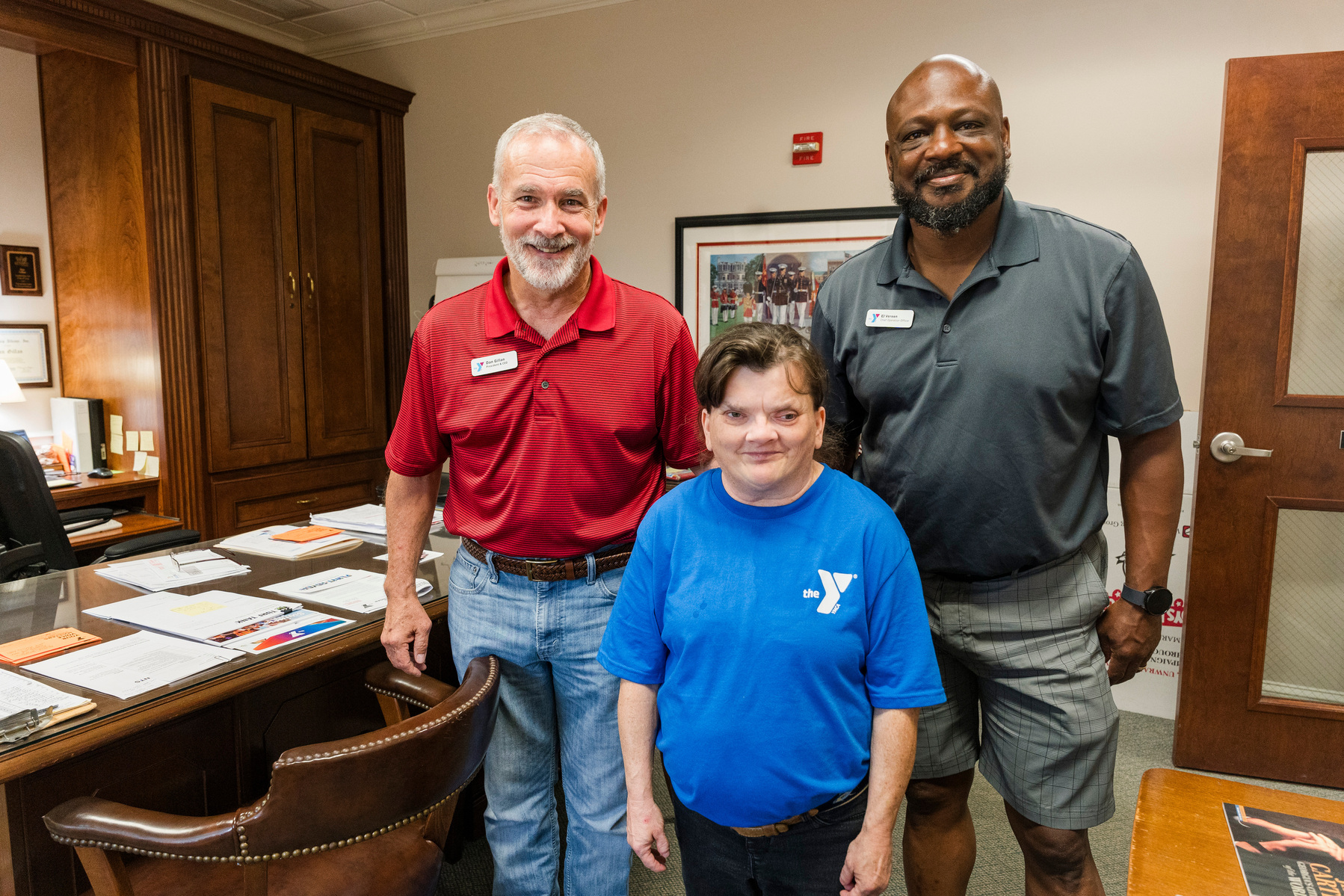 Three YMCA employees stand in an office and smile for the camera. 