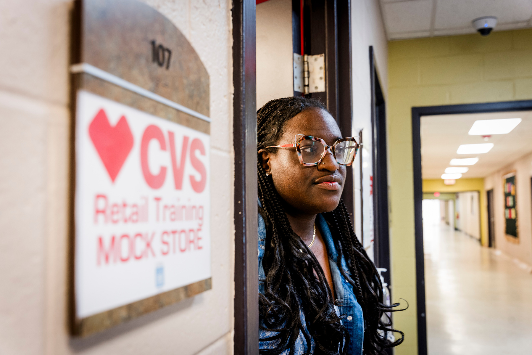 Young African American woman wears braids and stands next to the CVS Retail Training Classroom. 