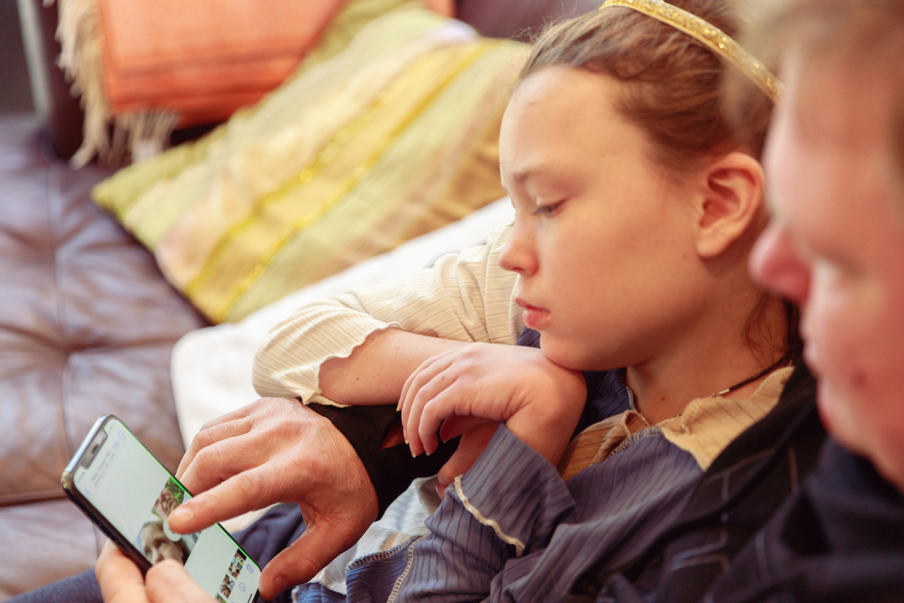 A young girl and her father sit on a sofa and look at a smartphone. 