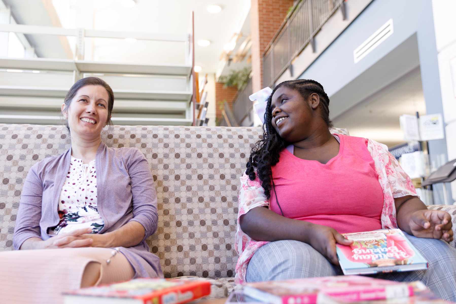 Mother and daughter sit on a patterned sofa and smile at each other. 