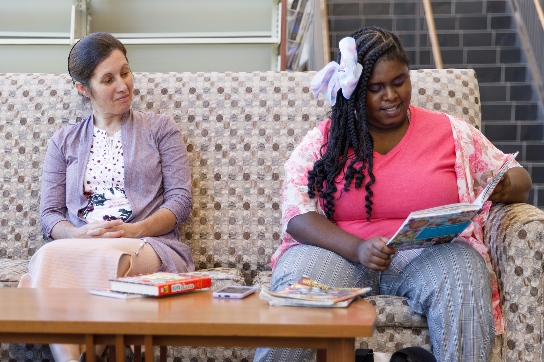 Mother and daughter sit on a patterned sofa and enjoy books.