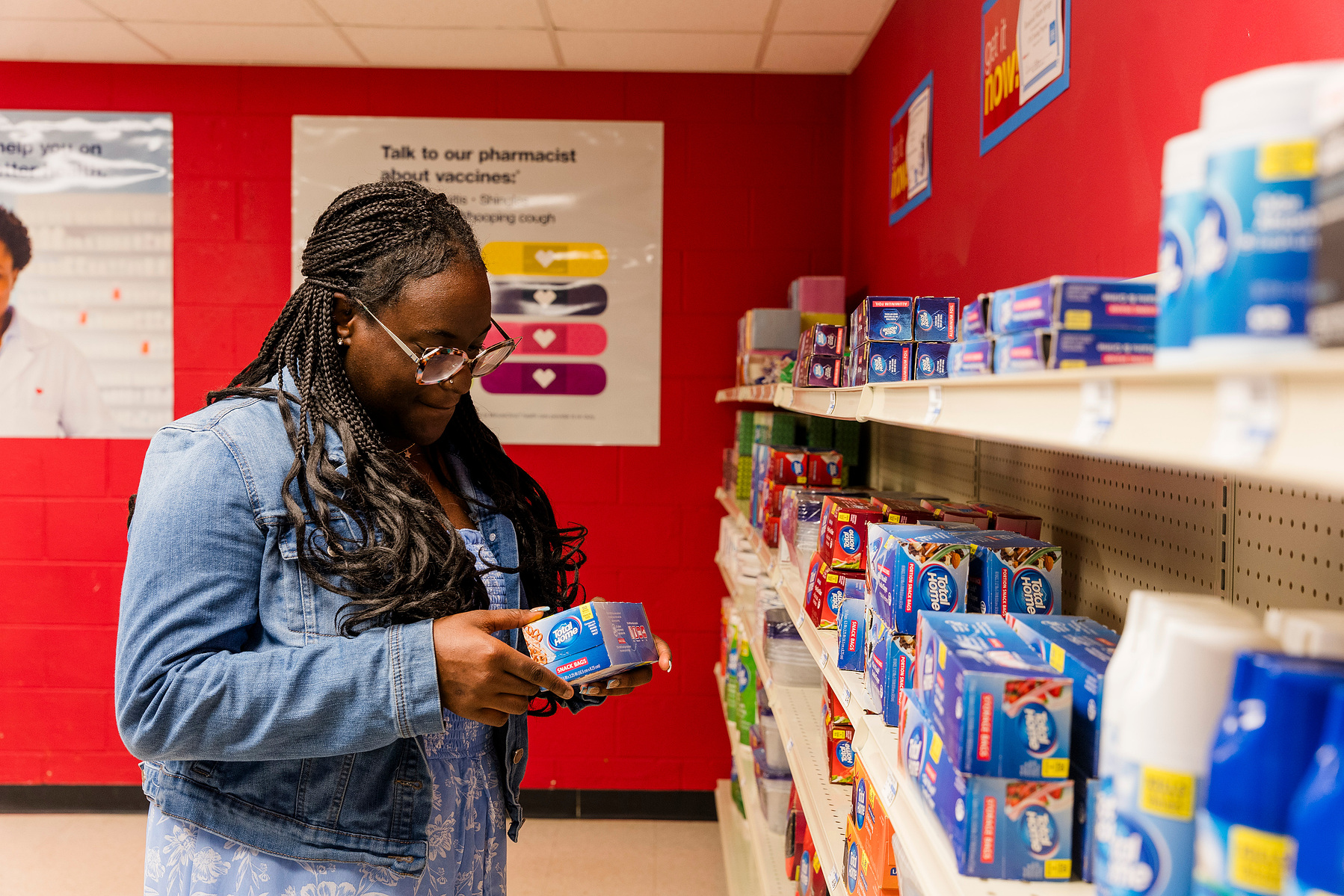 Young African American woman wears braids and looks at items on a shelf in a mock drug store. 
