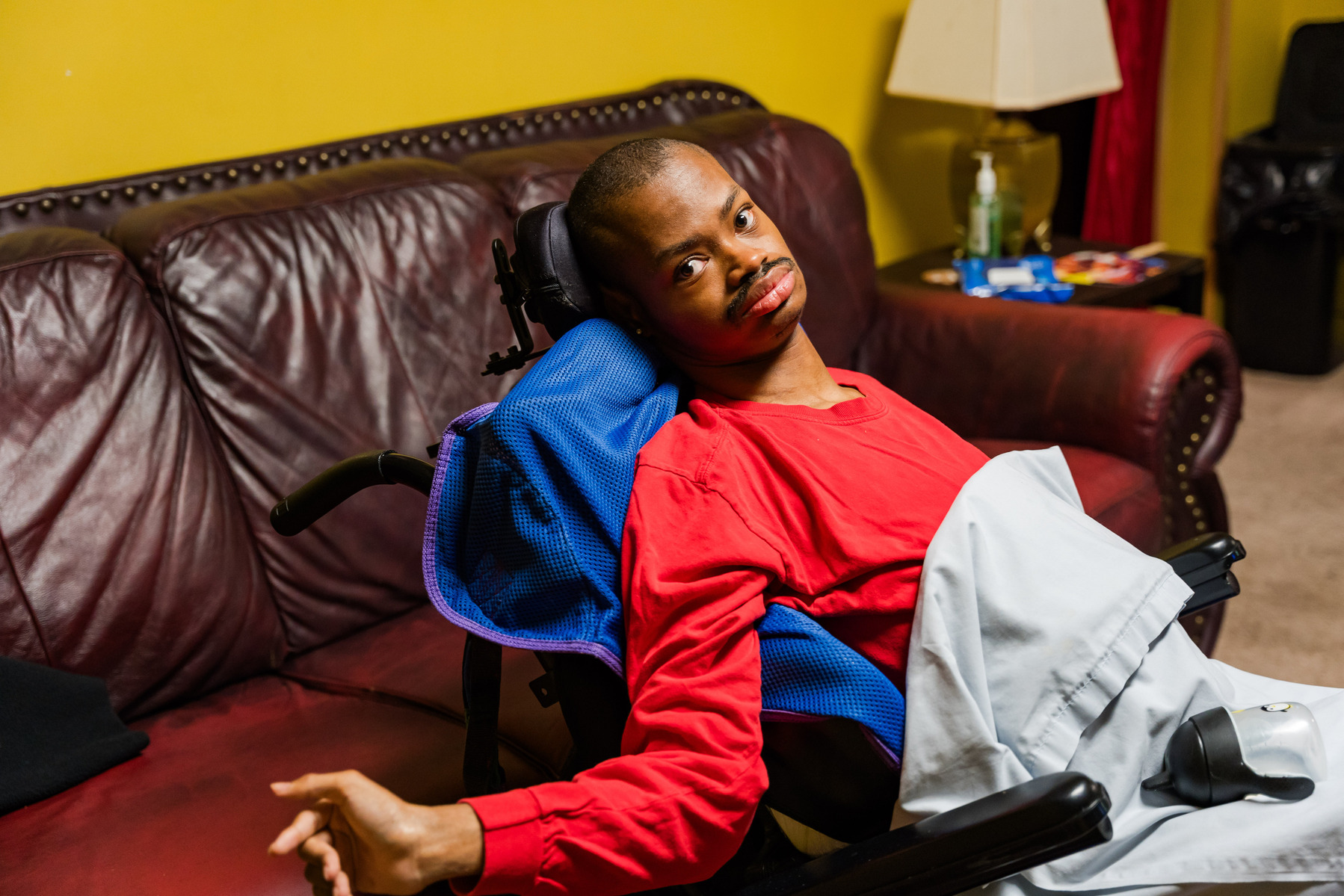 A young African American man wears a red shirt and sits in a wheelchair.