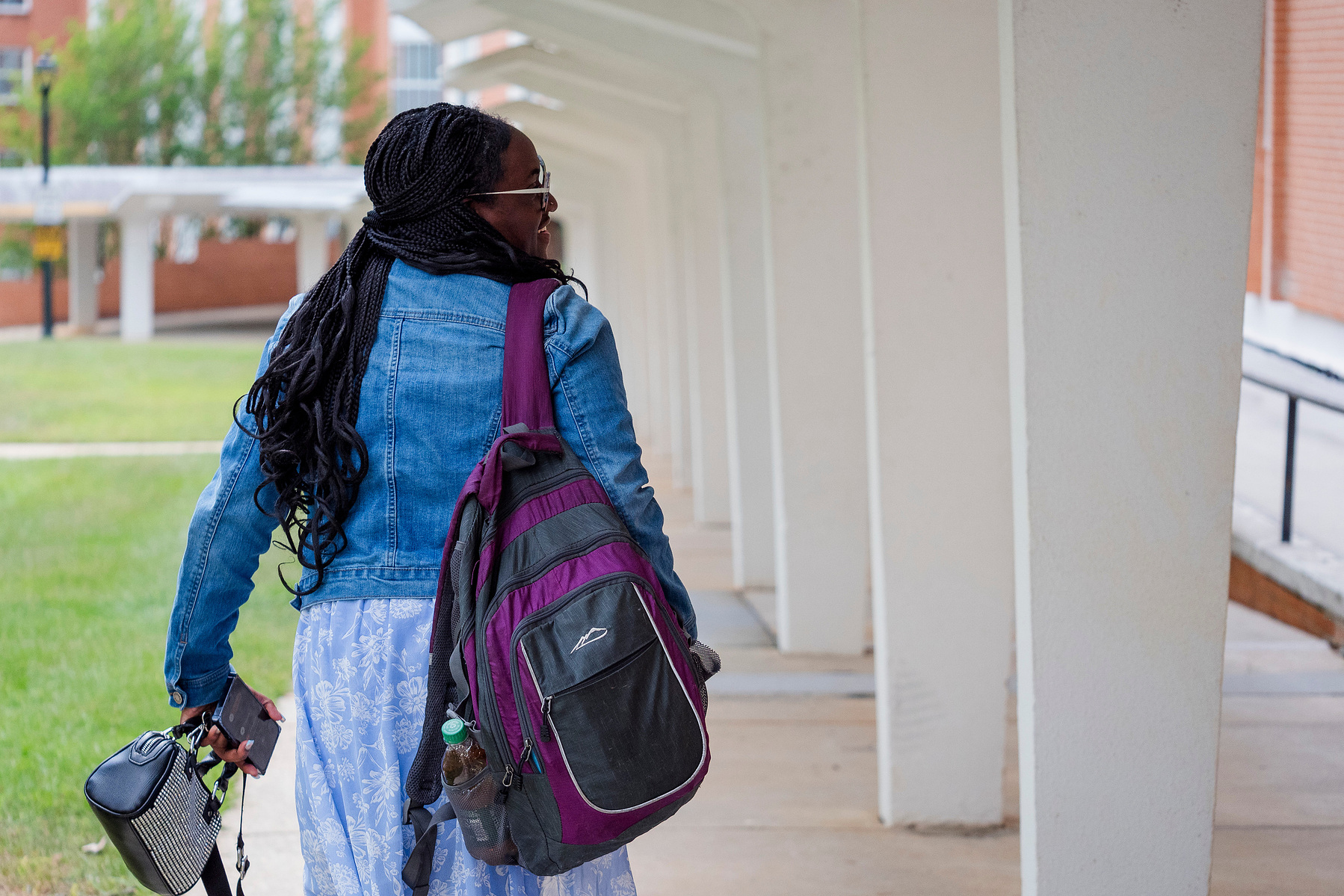 Young African American woman wears braids and walks down a walkway.