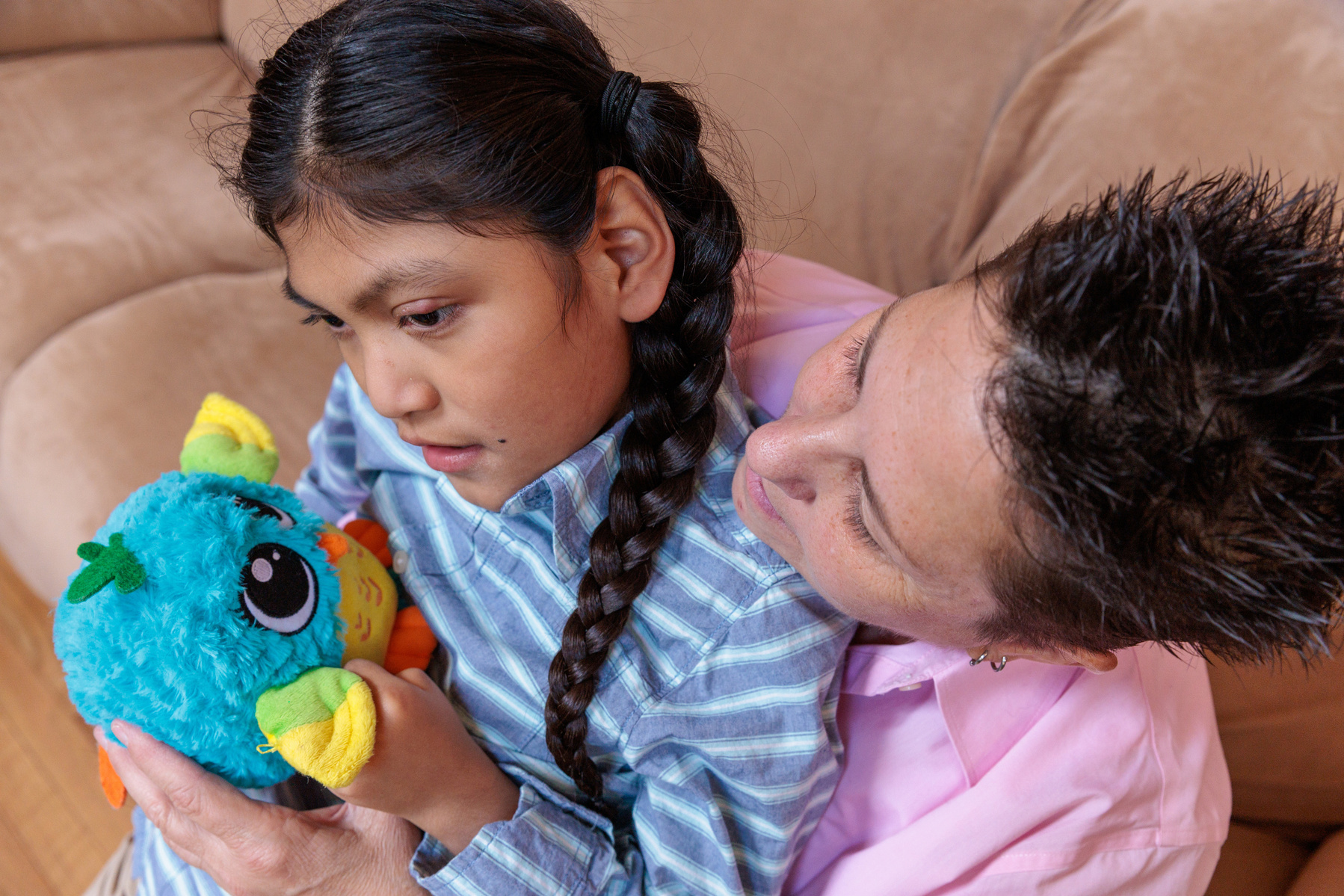 A boy with two long braids sits in his mother's lap and hols a toy.