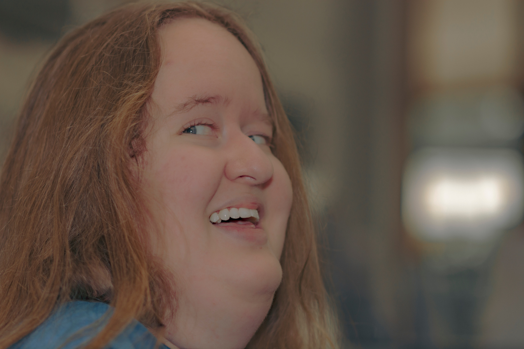 Woman with red hair wears a blue t-shirt and smiles at the camera over her shoulder. 