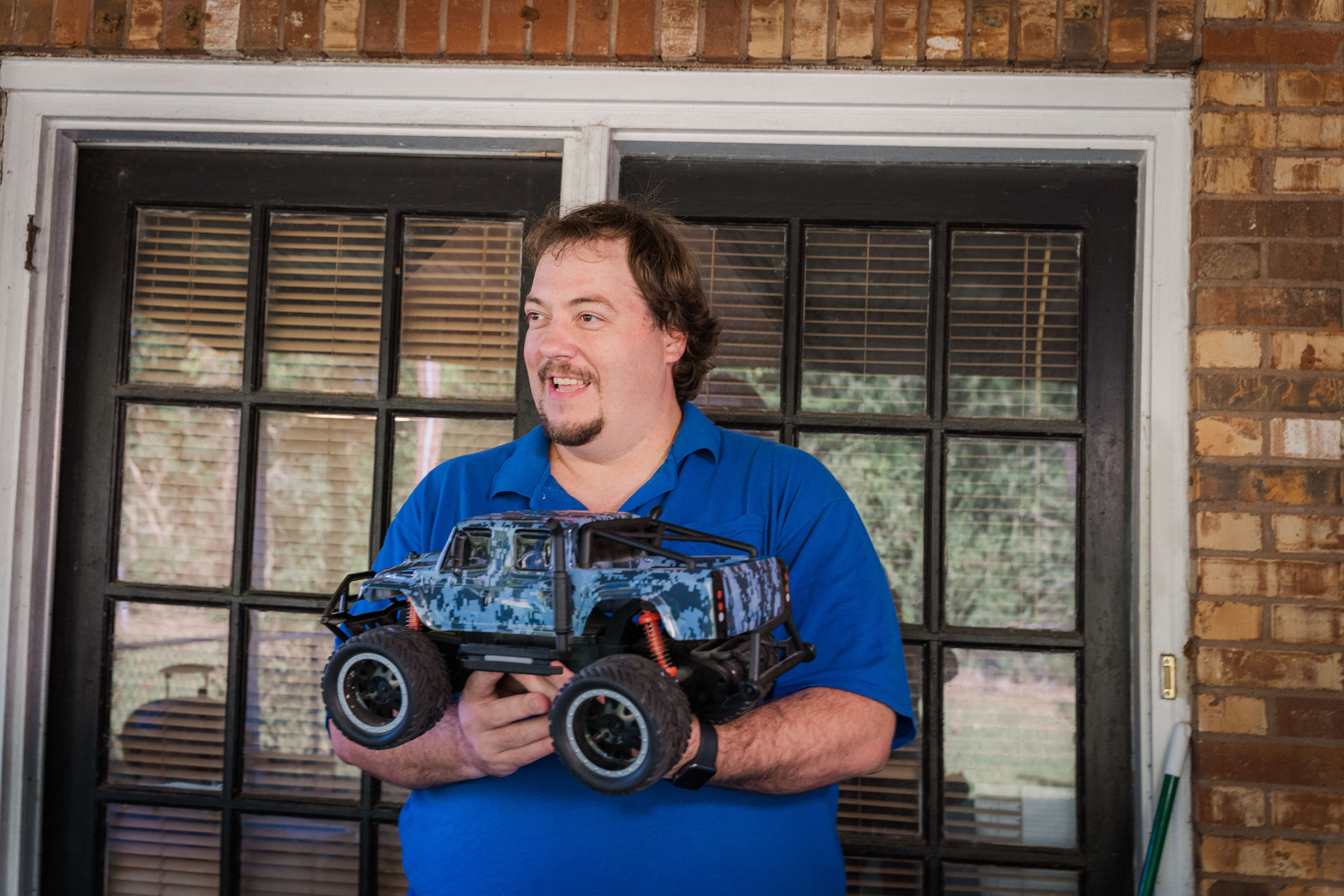 A man in a blue polo shirt holds a remote-controlled truck. 