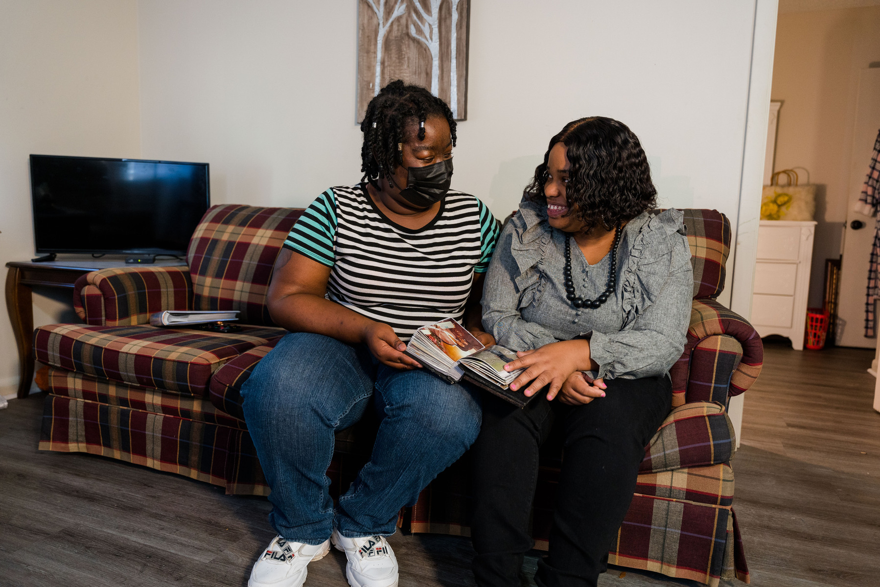Two women sit close together on a sofa inside a home. 