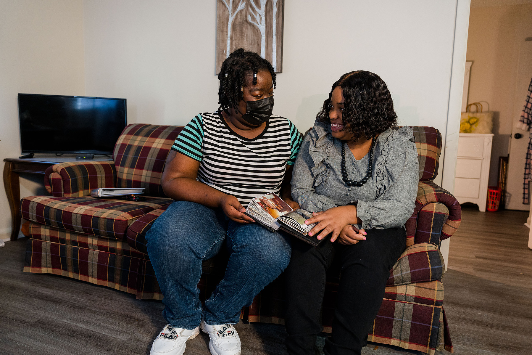 Two women sit close together on a sofa inside a home. 