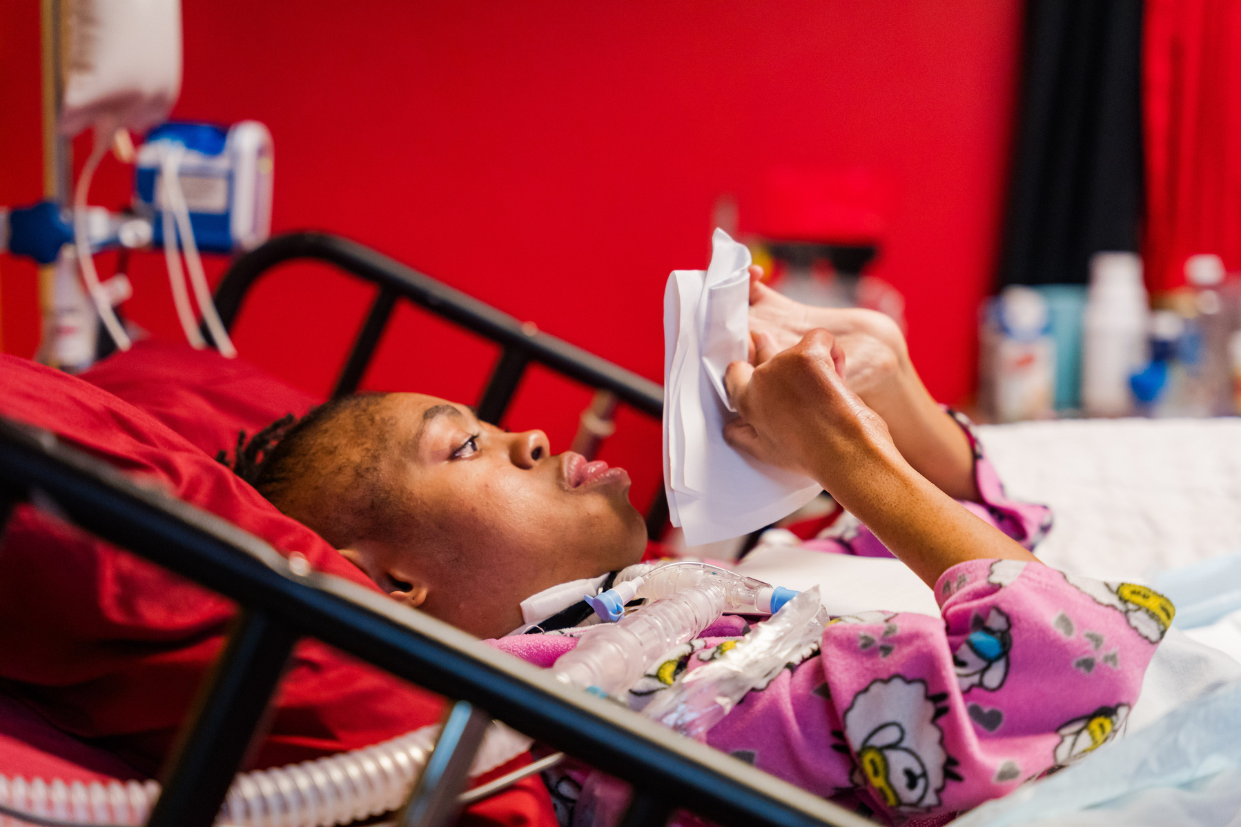 A young African American woman lies in a bed and folds paper. 