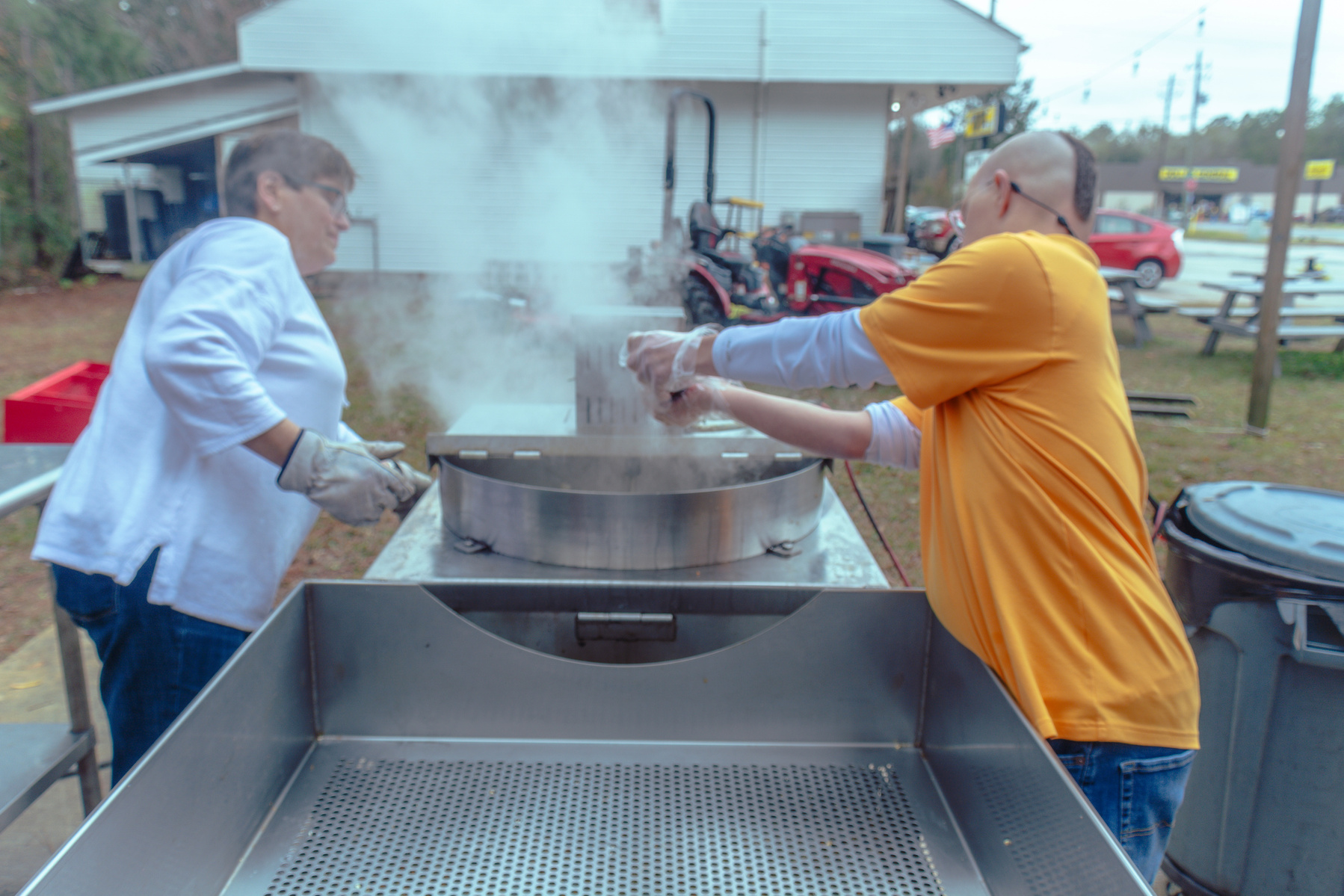 Two people dump popcorn from a steaming metal machine.