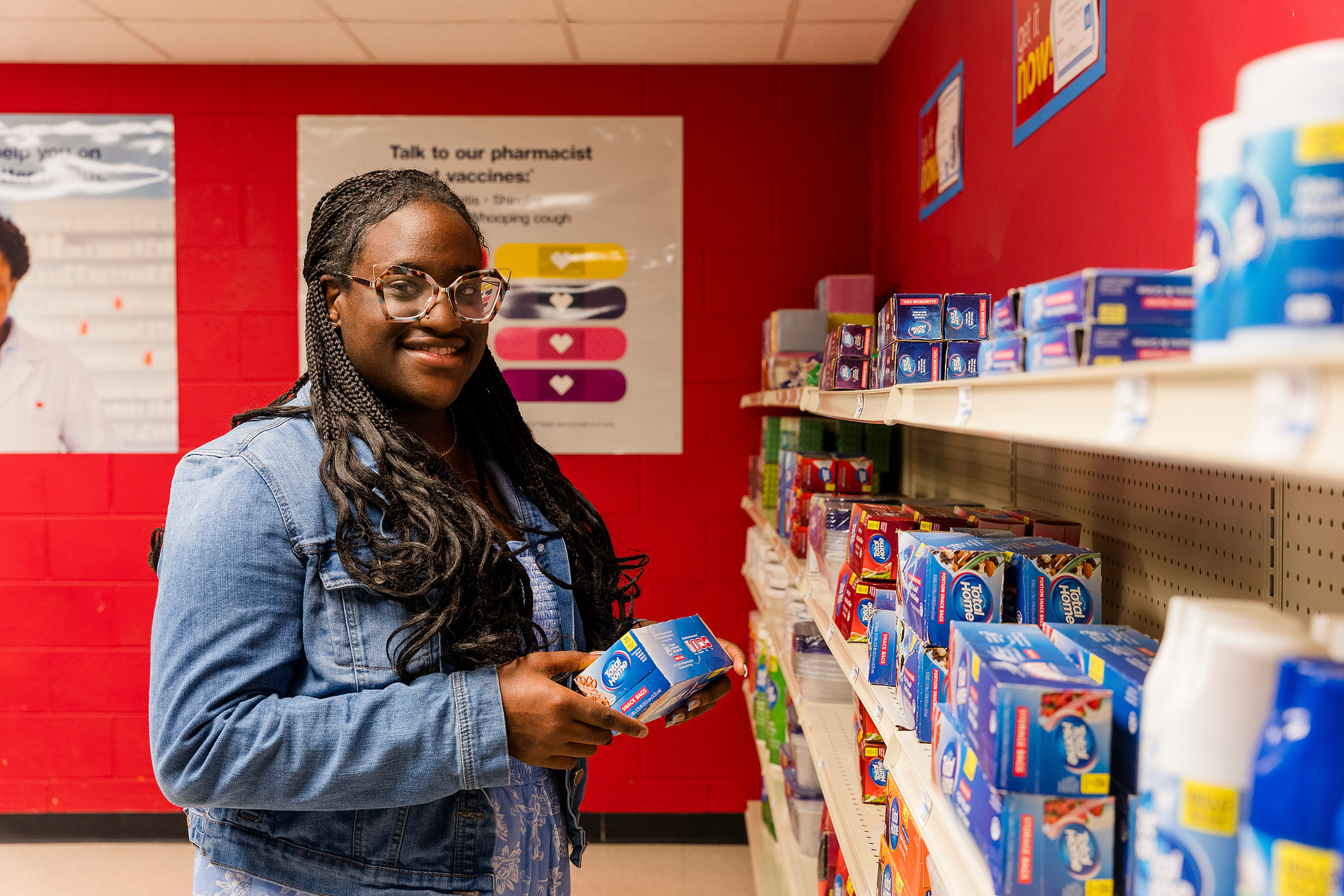 Young African American woman wears braids and looks at items on a shelf in a mock drug store. 