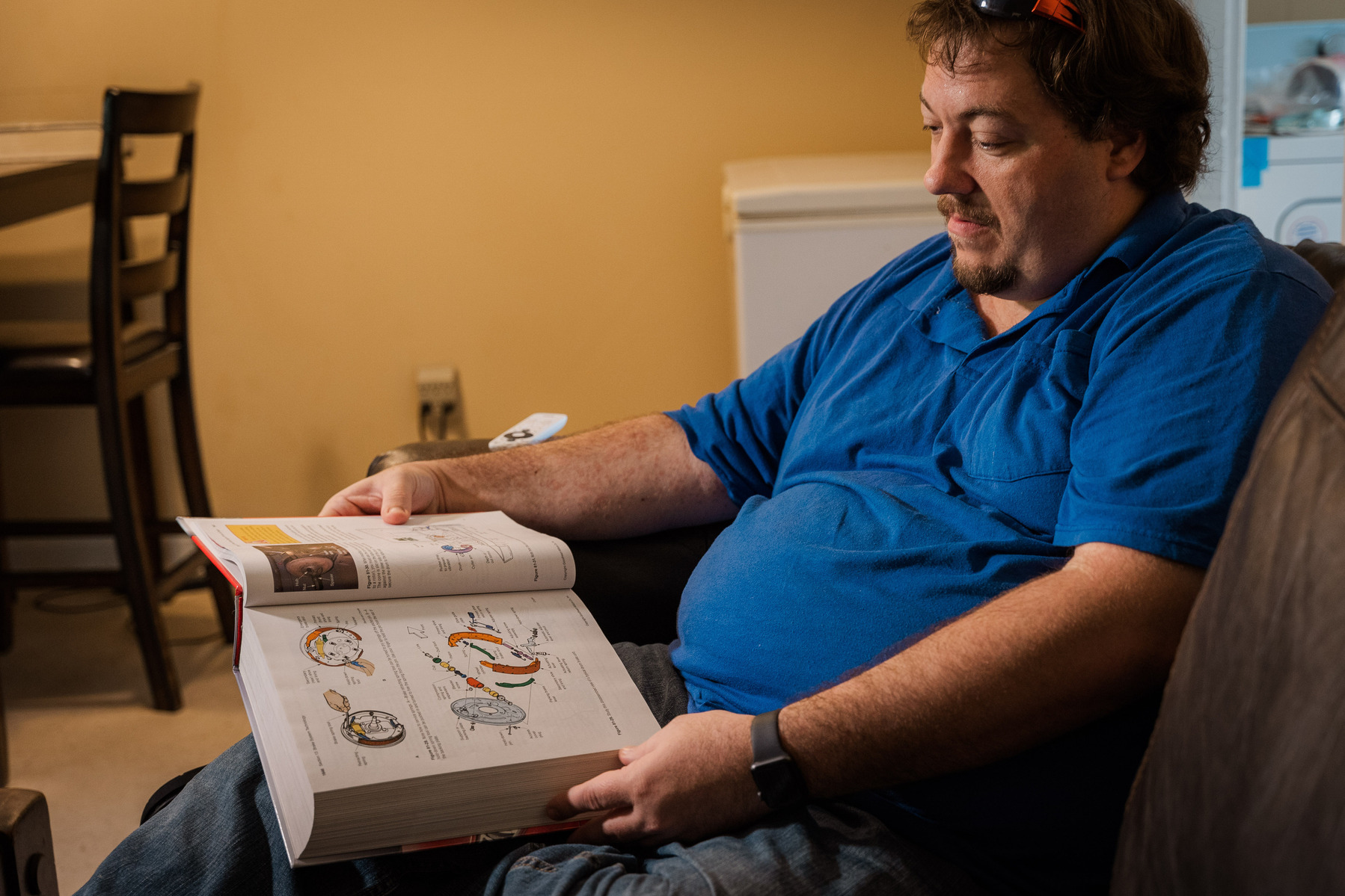 A man in a blue polo shirt looks at a book. 
