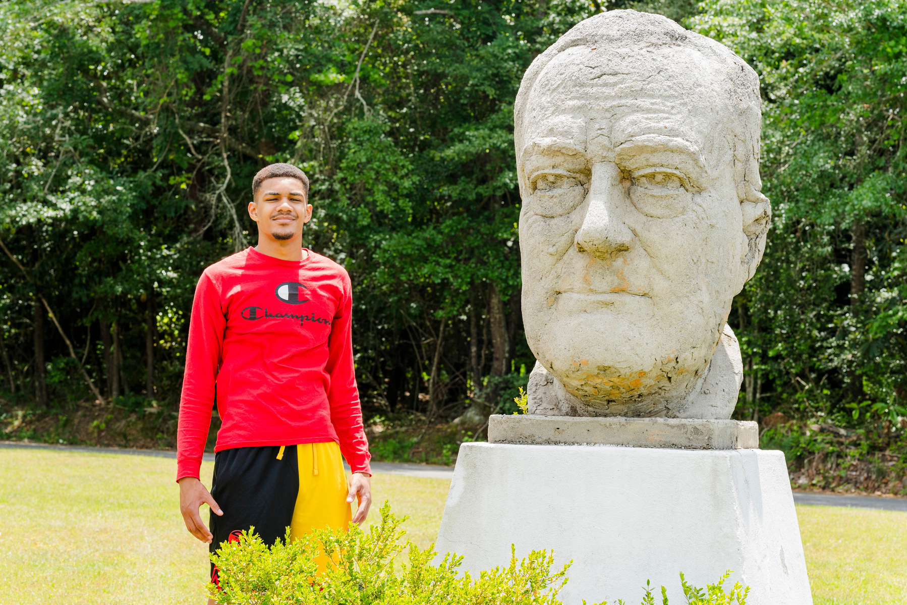 A young African American male stands next to a large sculpture of President Roosevelt.