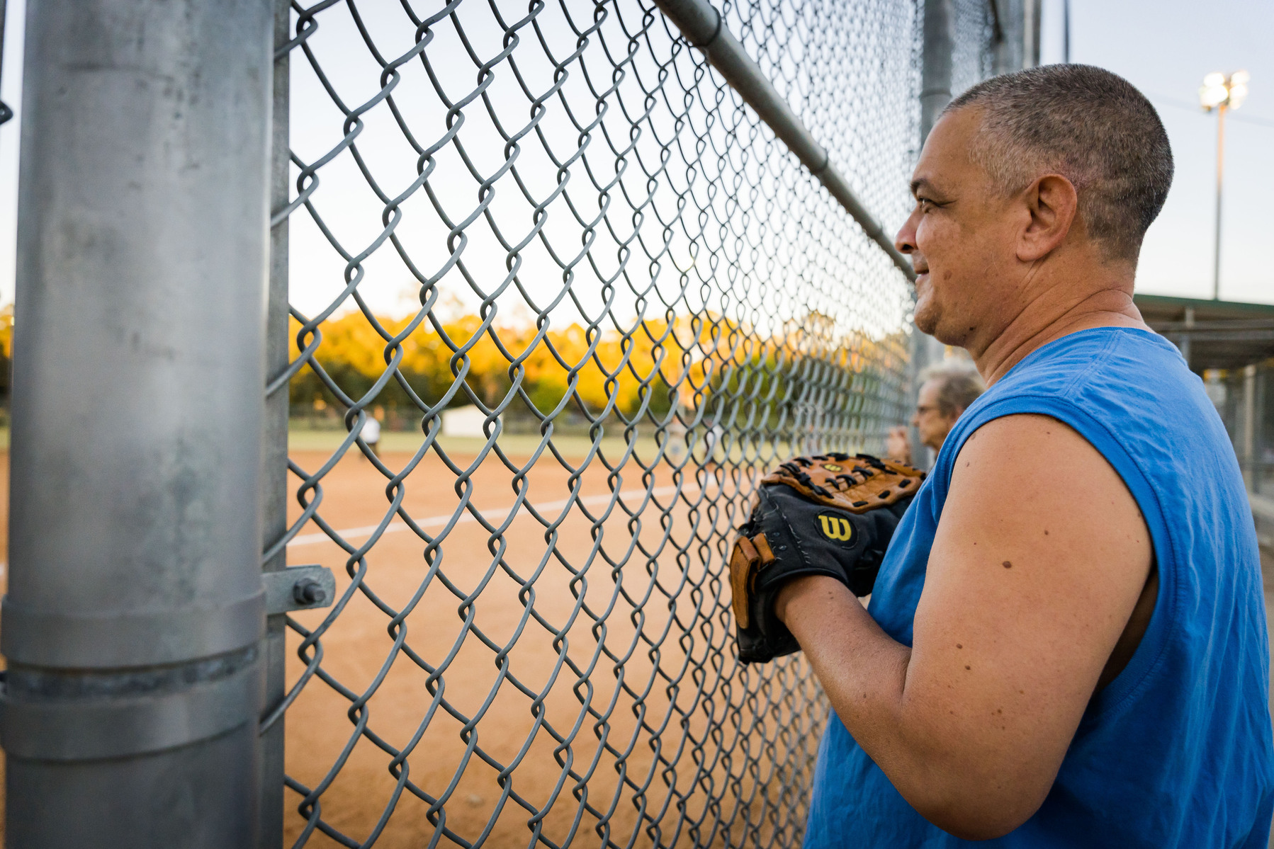 Man stands at fa ence with baseball glove.