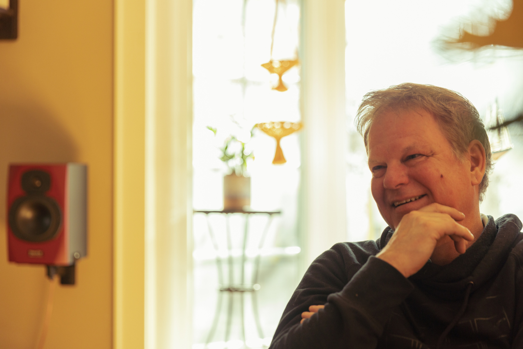 A middle aged man sits in front of a sun filled window. 