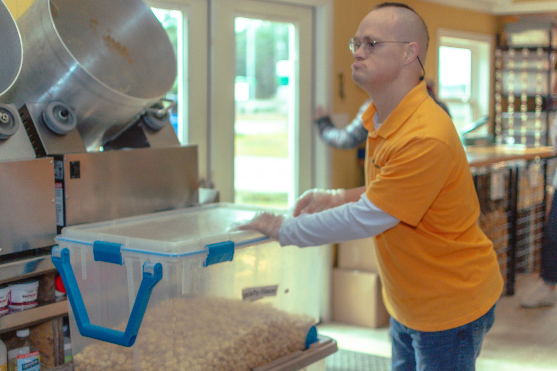 Man wears a yellow shirt as he places a clear bin on a table.