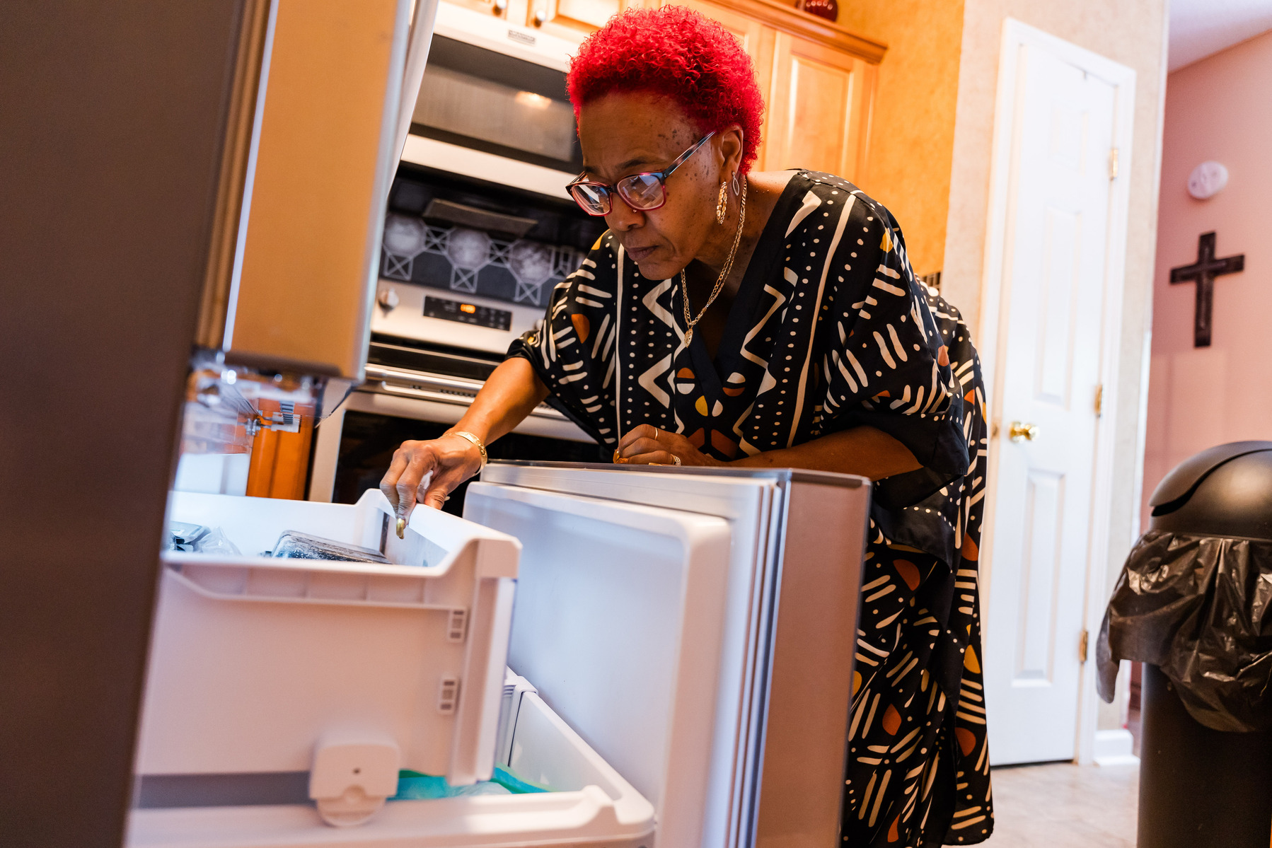 A woman with red hair looks into her refrigerator. 