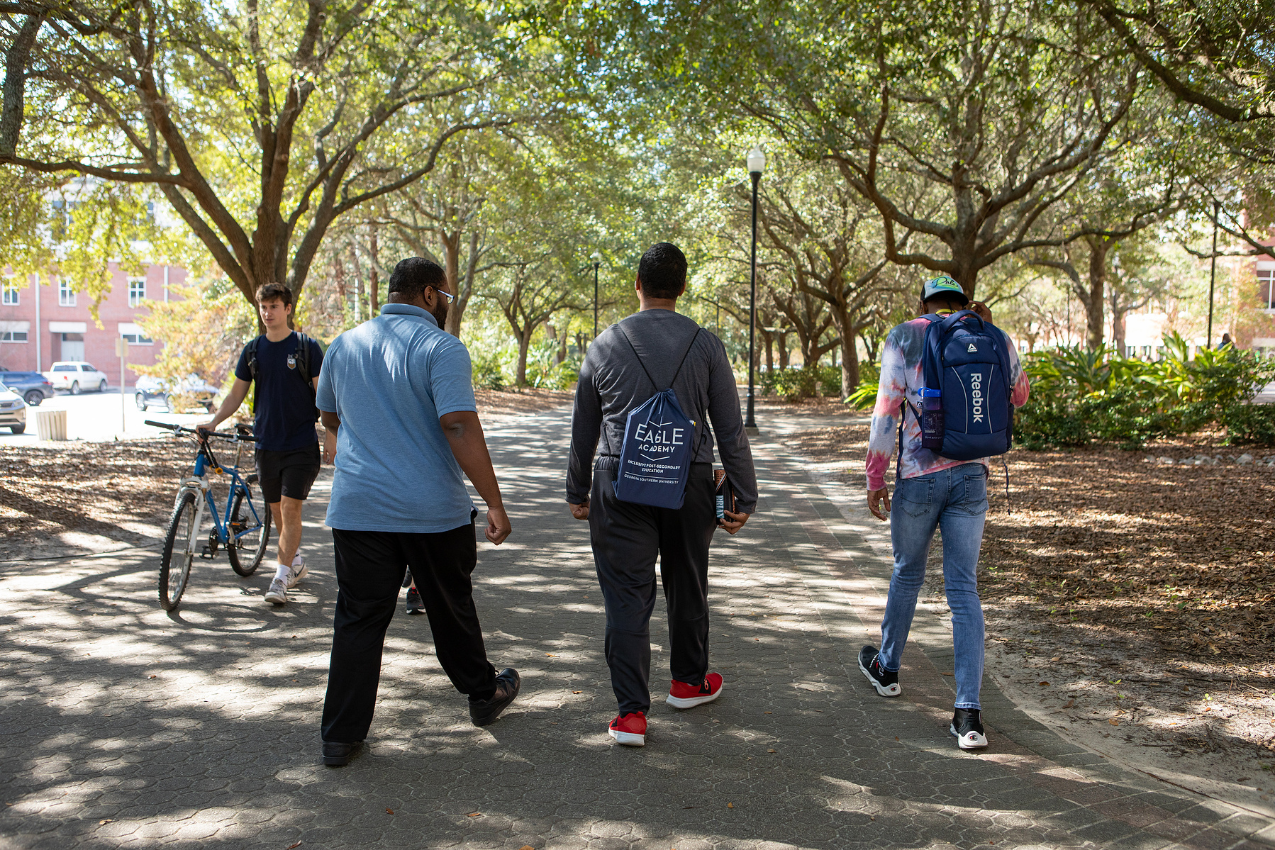 Three young men walk down a tree-lined path. 