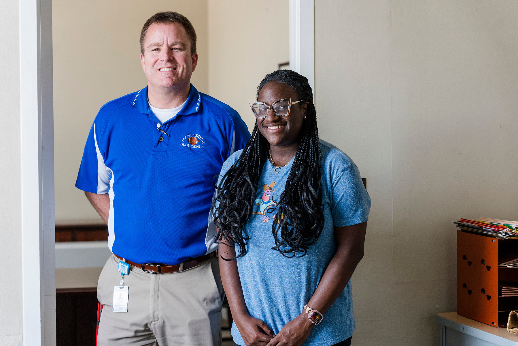 Young African American woman wears braids and stands with one of her instructors. 