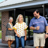 Four adults stand under an awning outside and smile for the camera. 