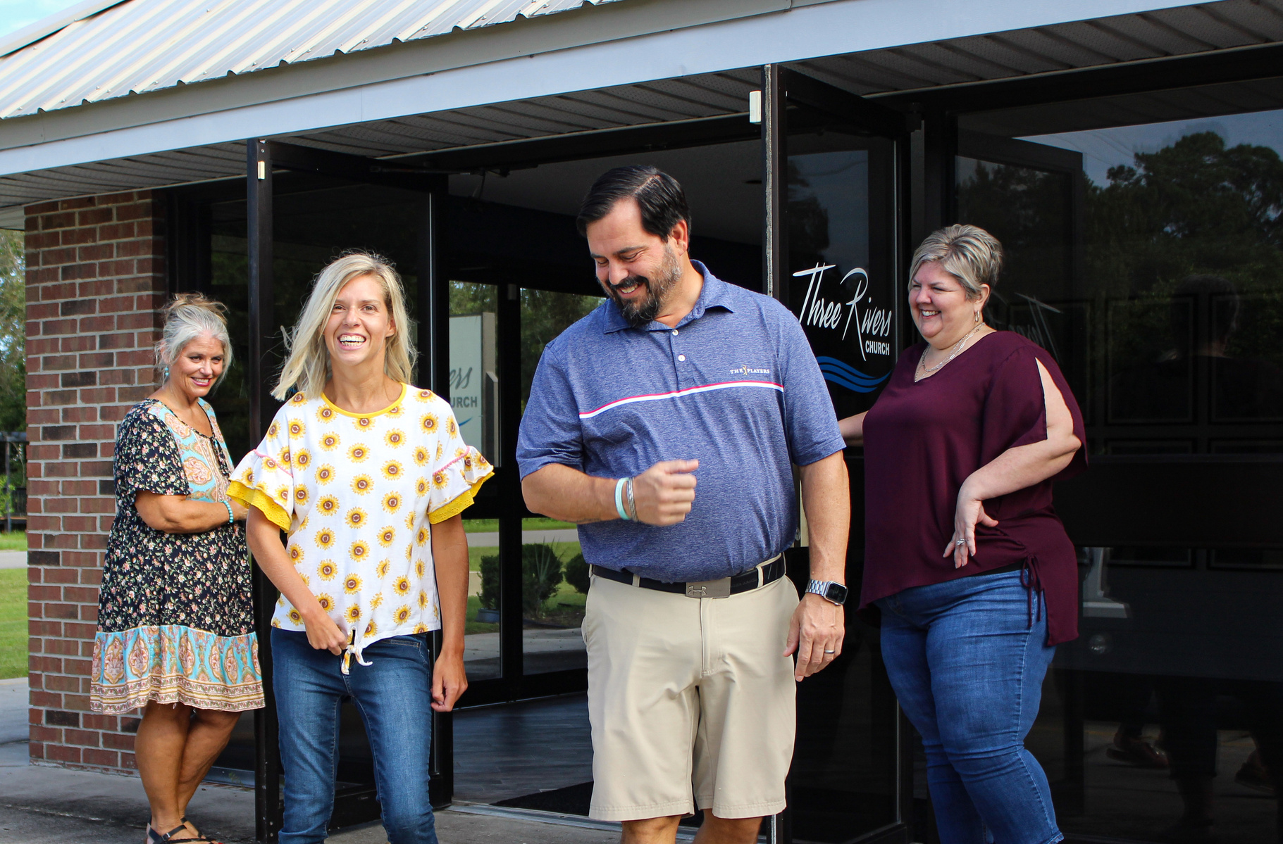 Four adults stand under an awning outside and smile for the camera. 
