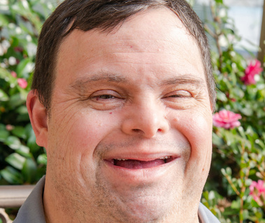 A man wearing a grey collared shirt smiles at the camera.
