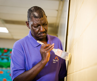 Two African American men wear matching purple polo shirts and sit at a table. 