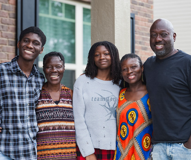 A family smiles for the camera as they stand in front of their home.