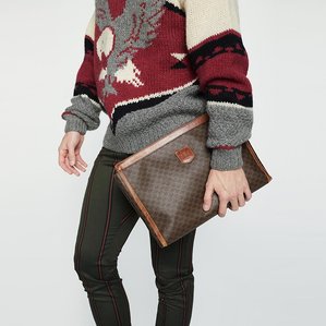 E-commerce catalogue image of male model, Mark Young, cropped, wearing a Vintage beige, maroon, and gray sweater with bald eagle design, olive and orange striped pants, holding a vintage 1970s 1980s brown Celine designer clutch bag