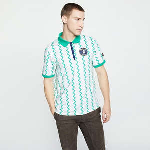 E-commerce catalogue image of male model, Mark Young, wearing a white and teal striped sports polo and brown skinny jeans standing in front of a white backdrop in-studio.