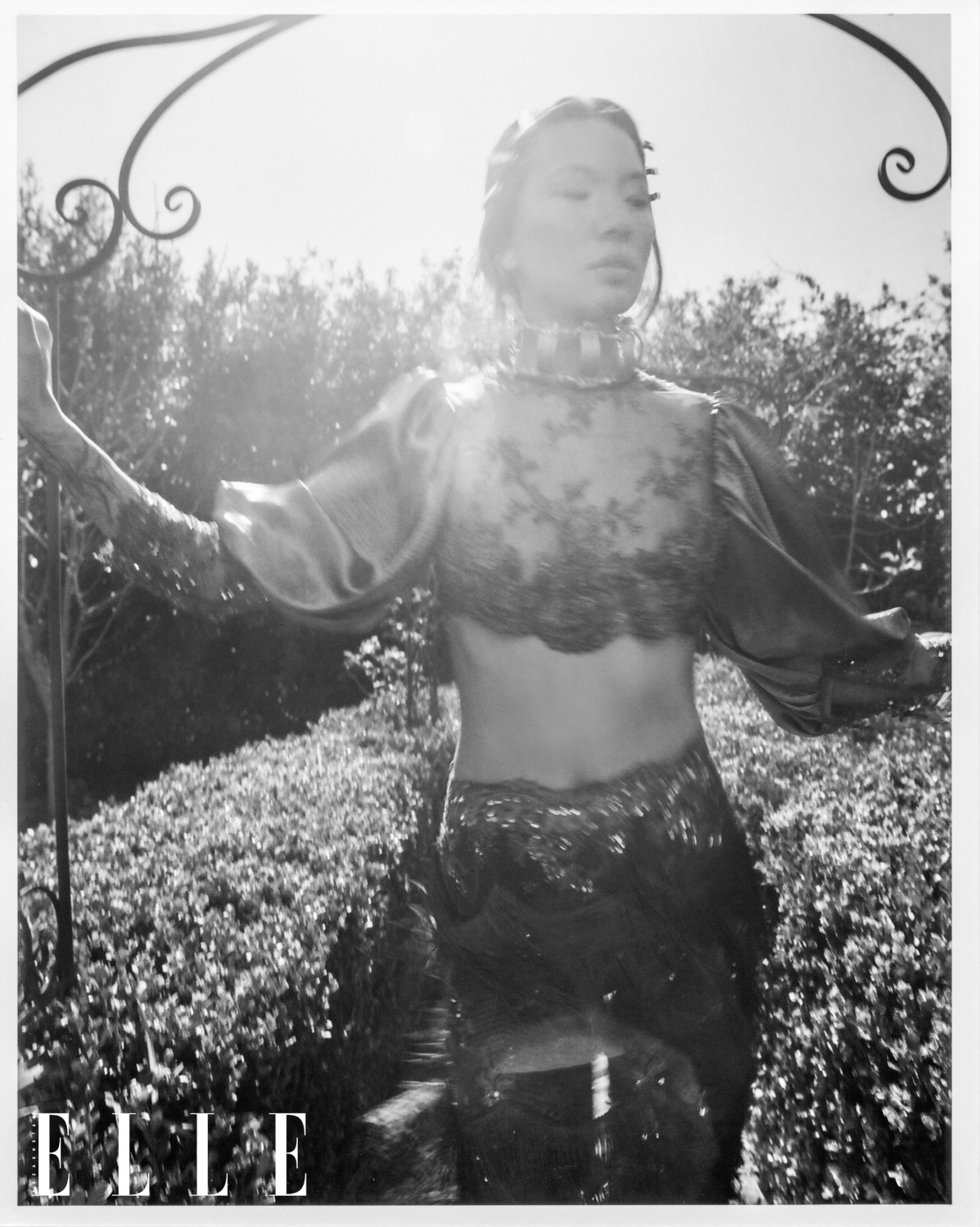 Black and white portrait of female Asian-American model Mei Li Zheng as she walks through a garden with the sun to her back. 
