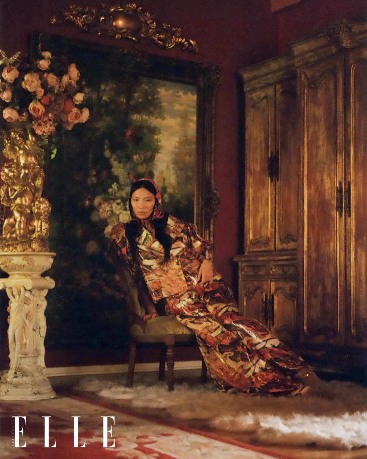 Asian-American female fashion model Mei Li Zheng bathed in a warm room light, sitting in a vintage baroque-era chair, wearing designer gold and red jacket and pants set, gold tiger striped shoes on top of a white fur carpet, floral arrangement next to her