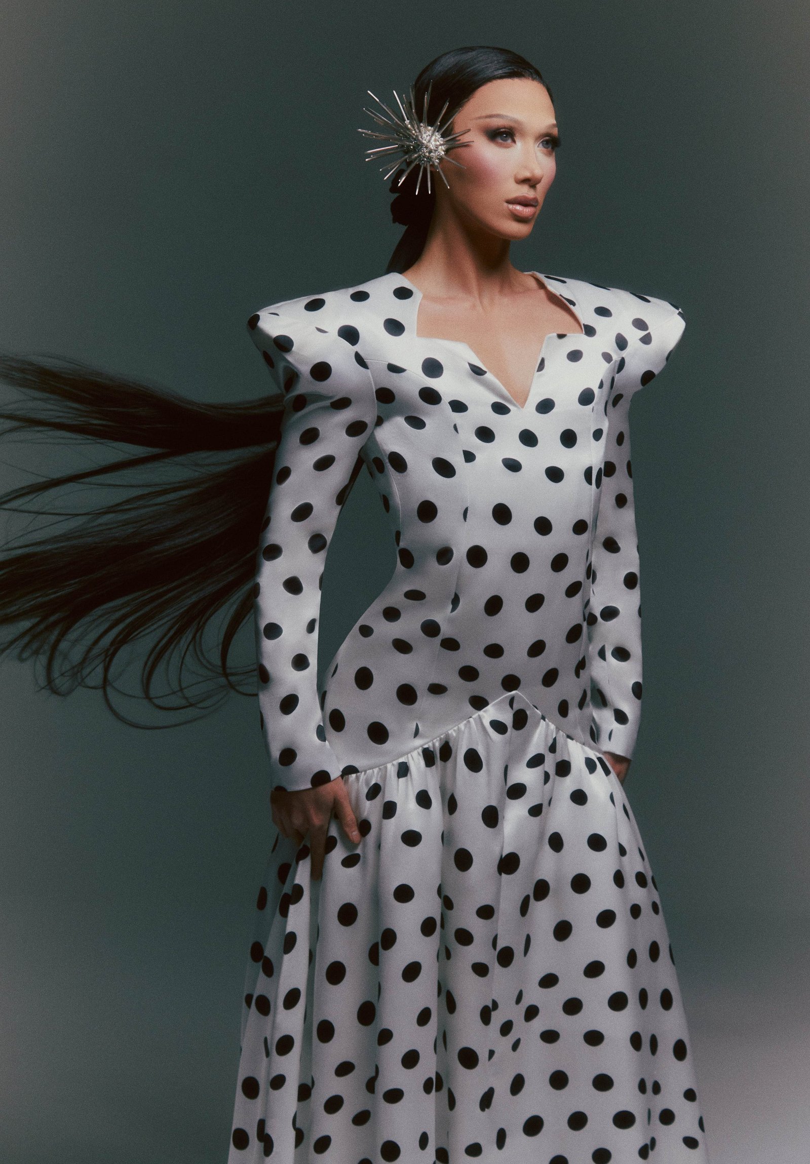 TikTok sensation and fan-favorite contestant of RuPaul's Drag Race, Vietnamese-American drag queen Plastique Tiara stuns in a  black and white polka dot dress with long black hair flowing in the wind.