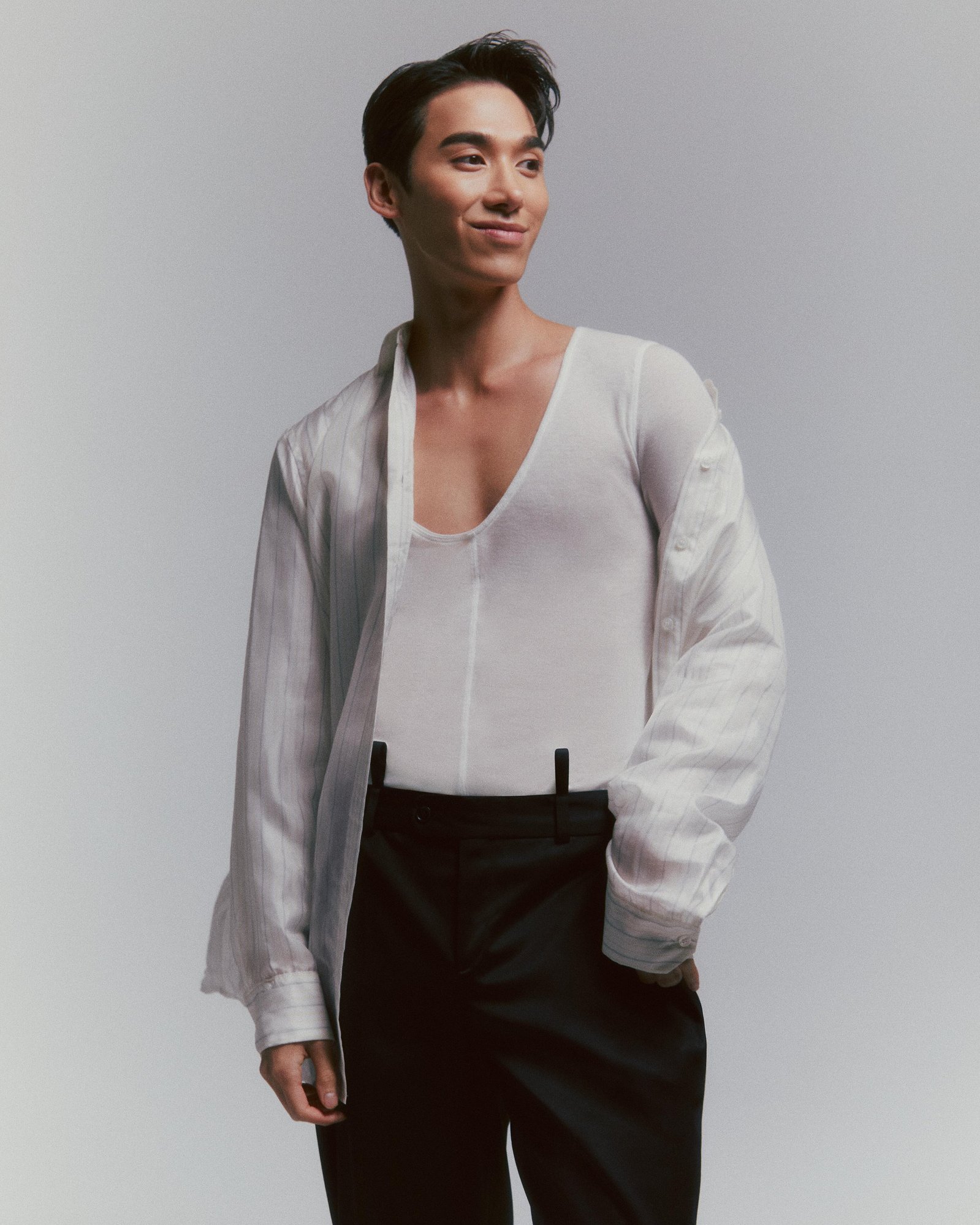 TikTok sensation and fan-favorite contestant of RuPaul's Drag Race, Vietnamese-American drag queen Plastique Tiara  out of drag, wearing a thin white v-neck cotton shirt, loose white dress shirt on top, and black trousers with protruding belt loops.