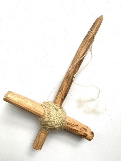 A handmade spindle made from tree branches and an elastic band with some spun wool on it.