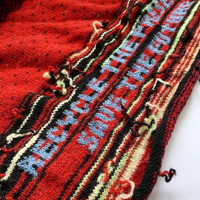 A part of a reknitted cardigan with a knitted text reading 'recycle the present, save the future'.